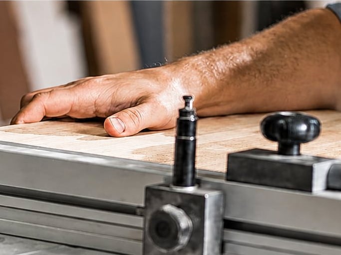 Un menuisier maintient à deux mains une planche de bois contre le guide d'une scie circulaire dans son atelier.