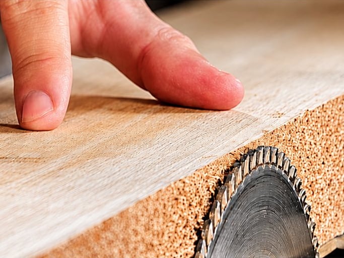 Gros plan sur les mains d'un menuisier guidant une planche de bois contre la lame d'une scie circulaire sur table.