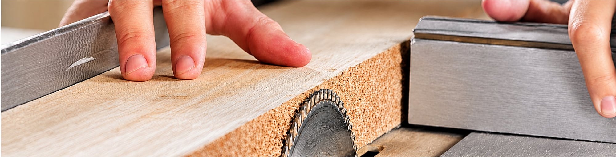 Gros plan sur les mains d'un menuisier guidant une planche de bois contre la lame d'une scie circulaire sur table.